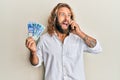 Handsome man with beard and long hair talking on the phone holding 100 brazilian reals angry and mad screaming frustrated and Royalty Free Stock Photo