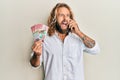 Handsome man with beard and long hair talking on the phone holding 100 new zealand dollars angry and mad screaming frustrated and Royalty Free Stock Photo