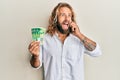 Handsome man with beard and long hair talking on the phone holding 50 shekels angry and mad screaming frustrated and furious, Royalty Free Stock Photo