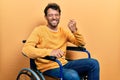 Handsome man with beard sitting on wheelchair celebrating surprised and amazed for success with arms raised and eyes closed