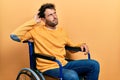 Handsome man with beard sitting on wheelchair confuse and wondering about question Royalty Free Stock Photo