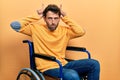 Handsome man with beard sitting on wheelchair doing funny gesture with finger over head as bull horns