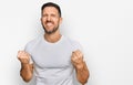 Handsome man with beard wearing casual white t shirt very happy and excited doing winner gesture with arms raised, smiling and Royalty Free Stock Photo
