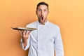 Handsome man with beard wearing chef uniform holding silver tray scared and amazed with open mouth for surprise, disbelief face Royalty Free Stock Photo