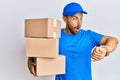 Handsome man with beard wearing courier uniform holding delivery packages looking at the watch time worried, afraid of getting Royalty Free Stock Photo