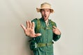 Handsome man with beard wearing explorer hat and backpack doing stop gesture with hands palms, angry and frustration expression