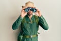 Handsome man with beard wearing explorer hat looking through binoculars clueless and confused expression Royalty Free Stock Photo
