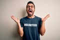 Handsome man with beard wearing t-shirt with volunteer message over white background celebrating mad and crazy for success with