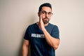 Handsome man with beard wearing t-shirt with volunteer message over white background hand on mouth telling secret rumor,