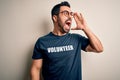 Handsome man with beard wearing t-shirt with volunteer message over white background shouting and screaming loud to side with hand