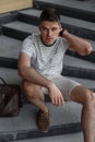 Handsome man with beautiful gray eyes with a stylish hairstyle in a fashionable T-shirt in trendy shorts with a leather bag Royalty Free Stock Photo