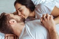 Handsome man and beautiful woman lying in bed and kissing in bedroom.