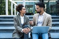 Handsome man and beautiful woman working on wireless laptop near office center. Two business people colleagues sitting on stairs Royalty Free Stock Photo