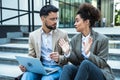 Handsome man and beautiful woman working on wireless laptop near office center. Two business people colleagues sitting on stairs Royalty Free Stock Photo