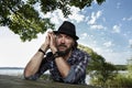 Handsome man with a black stylish hat sitting on a wooden bench in a beautiful natural parkland. happy man in his 40Ã¢â¬â¢s in the Royalty Free Stock Photo