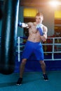 Handsome man in blue boxing gloves training on a punching bag in the gym. Male boxer doing workout. Royalty Free Stock Photo