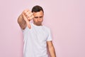 Handsome man with blue eyes wearing casual white t-shirt standing over pink background looking unhappy and angry showing rejection Royalty Free Stock Photo