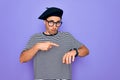 Handsome man with blue eyes wearing striped t-shirt and french beret over purple background In hurry pointing to watch time, Royalty Free Stock Photo