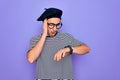 Handsome man with blue eyes wearing striped t-shirt and french beret over purple background Looking at the watch time worried, Royalty Free Stock Photo