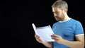 Handsome man in blue tshirt looking through papers. Cotract, bills, letter concepts. Black background