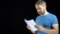 Handsome man in blue tshirt looking through papers. Cotract, bills, letter concepts. Black background. 4K video