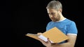Handsome man in blue tshirt looking through papers in yellow folder. Cotract, bills, checklist concepts. Black