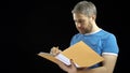 Handsome man in blue tshirt looking through papers in yellow folder and writing. Cotract, bills, checklist concepts