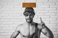 Handsome man builder with sexy muscular athletic strong body. Hard hat or helmet holds brick on white brick wall Royalty Free Stock Photo