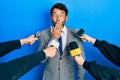 Handsome man business with beard being interviewed by reporters holding microphone covering mouth with hand, shocked and afraid
