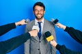 Handsome man business with beard being interviewed by reporters holding microphone looking positive and happy standing and smiling