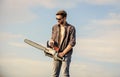 Handsome man with chainsaw blue sky background. Gardener lumberjack equipment. Lumberjack with chainsaw in his hands