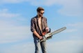 Handsome man with chainsaw blue sky background. Gardener lumberjack equipment. Lumberjack with chainsaw in his hands