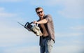 Handsome man with chainsaw blue sky background. Gardener lumberjack equipment. Sharp blade. Dangerous job. Feeling manly Royalty Free Stock Photo