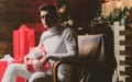 Handsome man with christmas gift. Portrait of a elegant mysterious stylish man in white clothing sitting in a chair