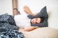 Handsome man covering his head and ears blocking out the sound with a pillow, suffering from loud alarm wake-up signal, young guy