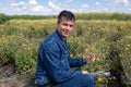 Handsome man crouching in marigold field holding flower looking at camera