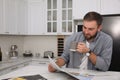 Handsome man with cup of coffee reading magazine at white marble table in kitchen Royalty Free Stock Photo