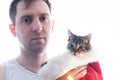 Man with dark hair holding cute brown tabby cat in red santa fur hat and looking at camera Royalty Free Stock Photo