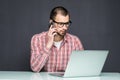 Handsome man dressed in shirt and talking on cellphone while using laptop over gray Royalty Free Stock Photo