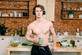 Handsome man drinking green smoothie in kitchen. Young man is listening to music in earphones, drinks smoothie while