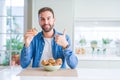 Handsome man eating chocolate chips muffin happy with big smile doing ok sign, thumb up with fingers, excellent sign Royalty Free Stock Photo