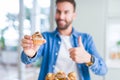 Handsome man eating chocolate chips muffin happy with big smile doing ok sign, thumb up with fingers, excellent sign Royalty Free Stock Photo