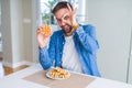 Handsome man eating sweet Belgian pancakes with happy face smiling doing ok sign with hand on eye looking through fingers Royalty Free Stock Photo