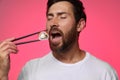 Handsome man eating tasty sushi roll with chopsticks on pink background Royalty Free Stock Photo