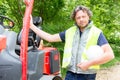 man engineer wearing protective uniform and hardhat smiling joyfully to the camera near forklift stacker