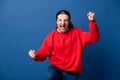 Handsome man excited doing winner gesture with arms, wearing casual red sweater very happy standing over isolated blue background,