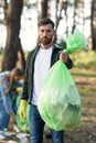 Good-looking bearded man shows a full rubbish pack in background of his friends volunteers picking up rubbish at park. Royalty Free Stock Photo