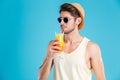 Handsome man in hat and sunglasses drinking fresh orange juice Royalty Free Stock Photo