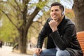 Handsome man with headphones listening to music while sitting on bench in park, space for text Royalty Free Stock Photo