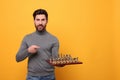 Handsome man holding chessboard with game pieces on yellow background. Space for text Royalty Free Stock Photo